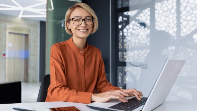 Woman with a friendly smile, working at a laptop.