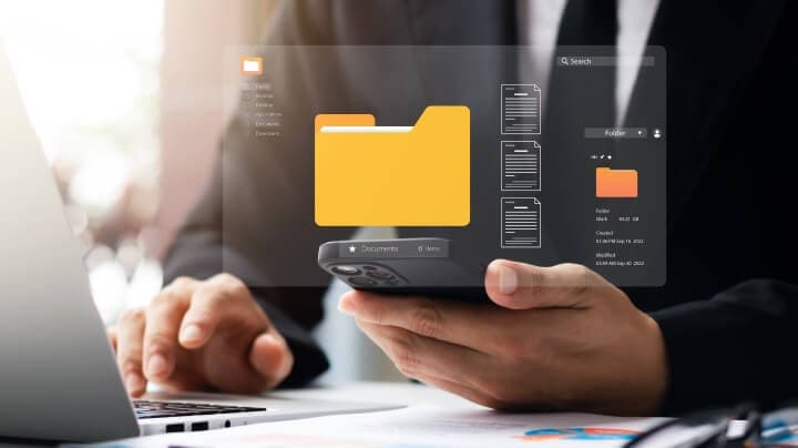 A person holding mobile phone and accessing digital folder in laptop