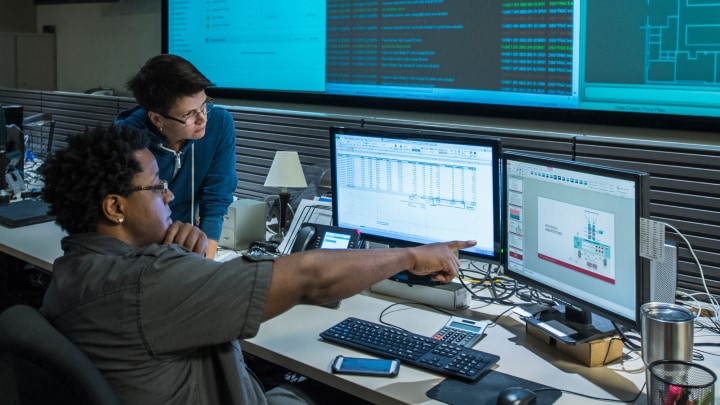 Two people working on multiple computer screens