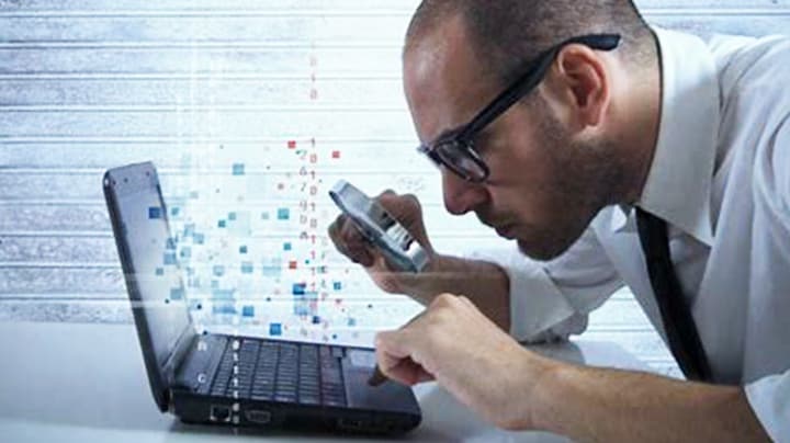 Person reviewing forensic data on a laptop with a magnifying glass
