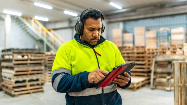 Warehouse worker wearing safety gear using a tablet inside a warehouse.