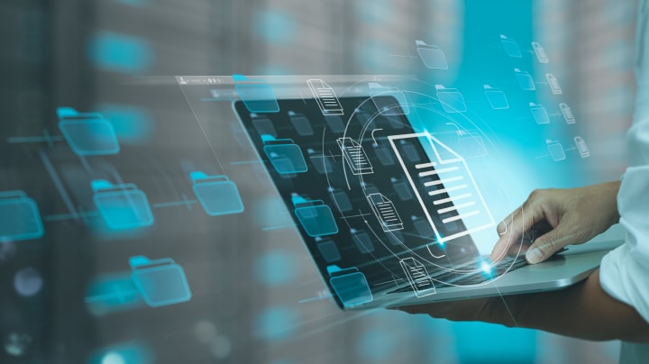 Person using a laptop with digital file and folder icons displayed holographically