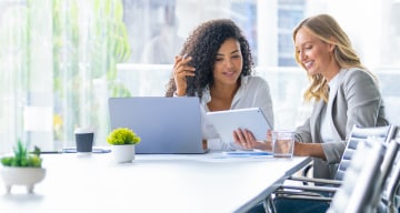 Two employees looking at computer and tablet together in conference room