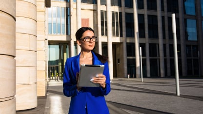 A person standing in front of a building holding a tablet/ipad