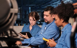 3 people working on a machinery in a factory and noting down information on a electronic device