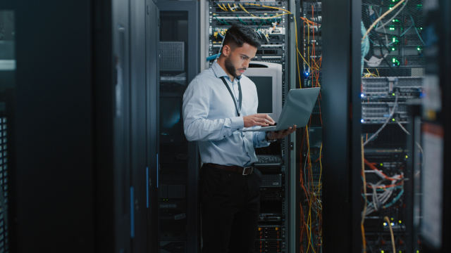 A system administrator working in server room using laptop