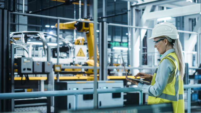 A person typing on laptop inside a manufacturing facility