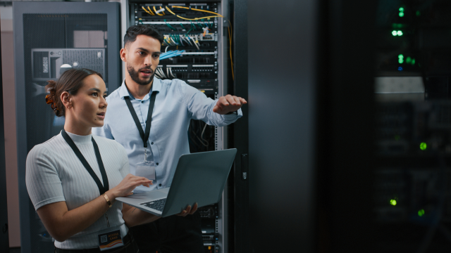 Two people are working on laptops in the data center