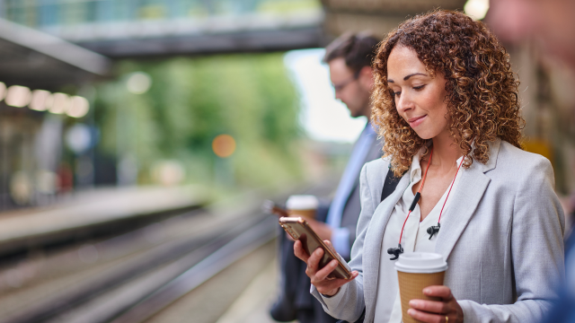 The person holding a cup of coffee while using a mobile phone