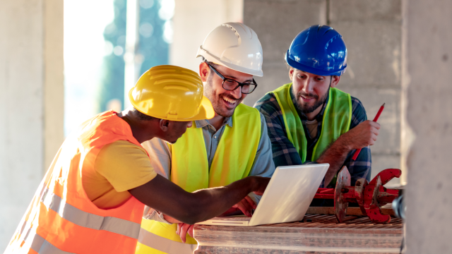 Three construction workers looking at a laptop