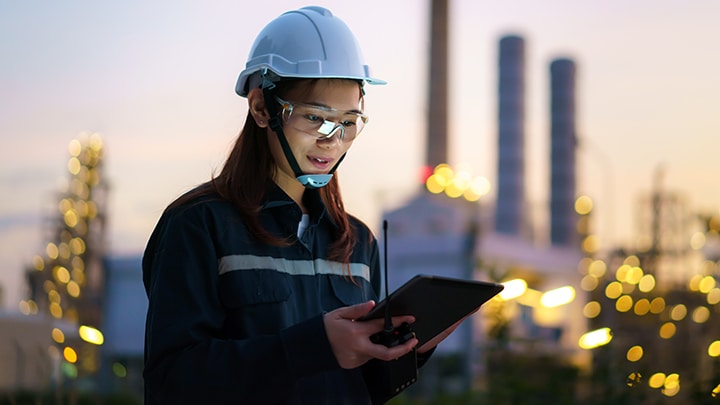 Man and woman in hard hats and safety jackets looking at tablet in industrial environment