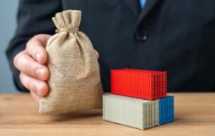 Person holding money bag beside shipping containers.